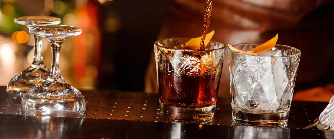 Ein Drink wird in ein Glas mit Eis und Orangenzeste gegossen. So trinkt man Whisky.