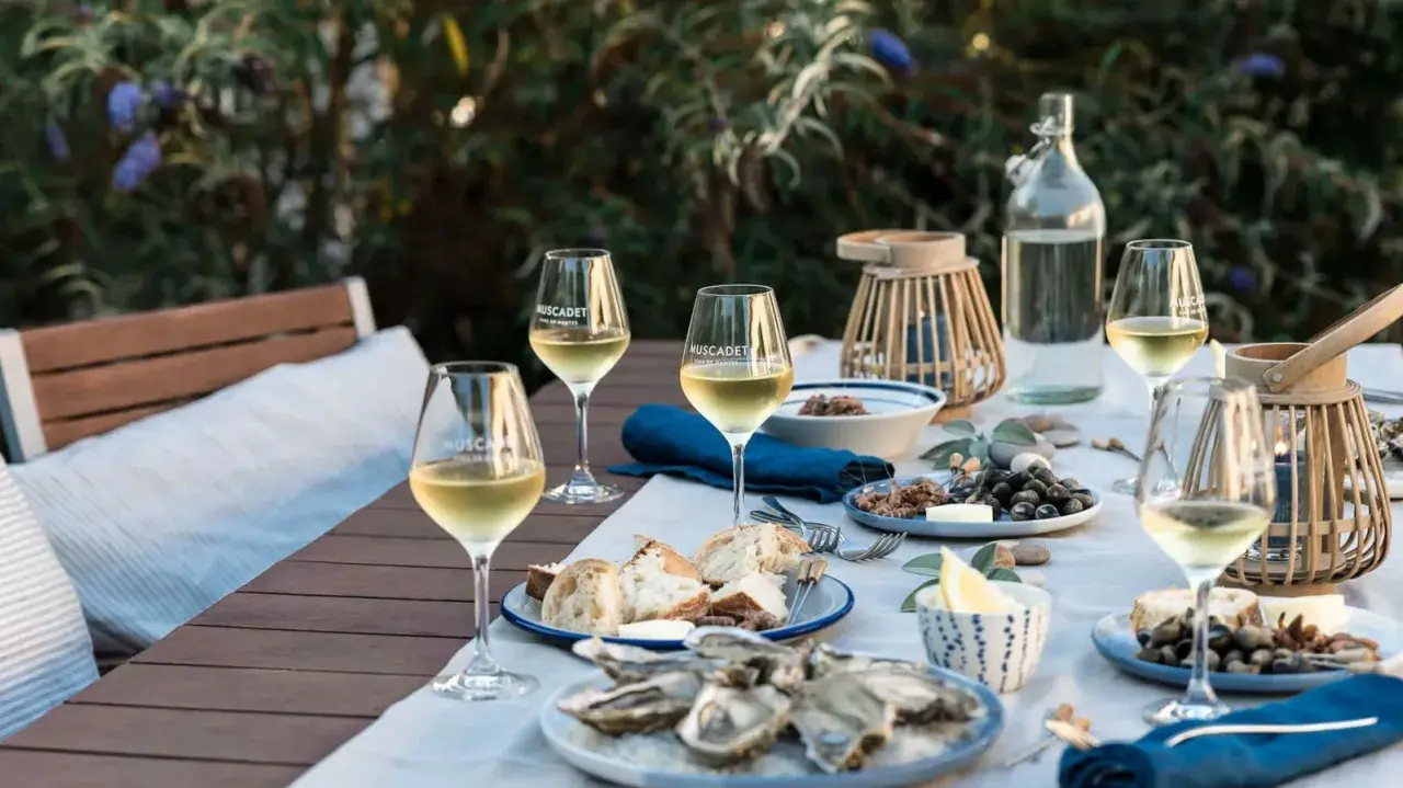 Ein gedeckter Tisch im Freien mit Austern, Brot und Gläsern voller Muscadet, einem Wein aus der Melon de Bourgogne Traube.