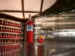 Eine Flasche Campari und ein Glas mit dem roten Aperitif stehen auf einer glänzenden Theke. Die Frage "wie schmeckt Campari?" wird durch den Anblick des ikonischen Getränks aufgeworfen.