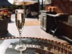 Ein Glas Sekt auf einem Tisch im Freien. Auch wenn Sekt kein Verfallsdatum hat, sollte er frisch genossen werden.