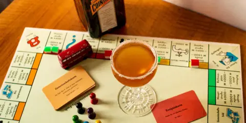 Ein Sidecar Cocktail steht auf einem Monopoly-Spielbrett neben einer Flasche Cointreau.
