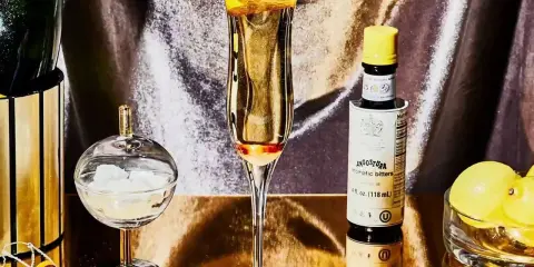 Elegantes Glas mit einem Champagner-Cocktail, garniert mit Zitronenschale. Daneben eine Flasche Angostura, Zuckerwürfel und Zitronen.