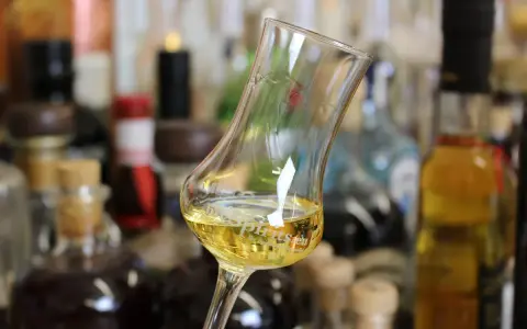 Ein Glas mit goldgelbem Wein steht vor einer Sammlung von Flaschen. Das Glas erinnert an ein Kirchenfenster, das Licht bricht.