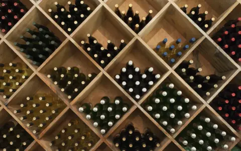 Holzregal mit vielen Flaschen Wein, ideal zum rotwein lagern. Verschiedene Sorten und Farben sind zu sehen.