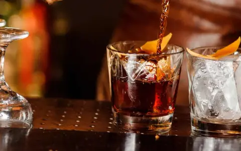 Ein Drink wird in ein Glas mit Eis und Orangenzeste gegossen. So trinkt man Whisky.