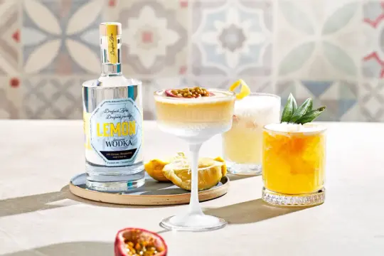 Erfrischender Vodka Sour mit Passionsfrucht und Zitrone, daneben ein weiterer Cocktail mit Ananas. Eine Flasche Zitronen-Wodka steht bereit.