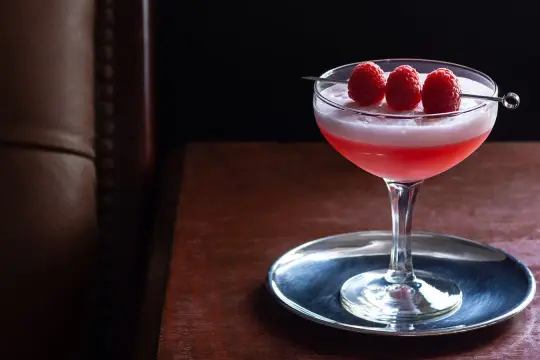 Ein eleganter Clover Club Cocktail mit Himbeeren auf einem silbernen Untersetzer, bereit zum Genuss.
