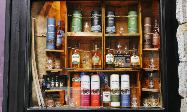 Regale voller irischer Whiskeys, darunter Connemara peated whisky, Kilbeggan und Tyrconnell. Gläser und Flaschen sind kunstvoll arrangiert.