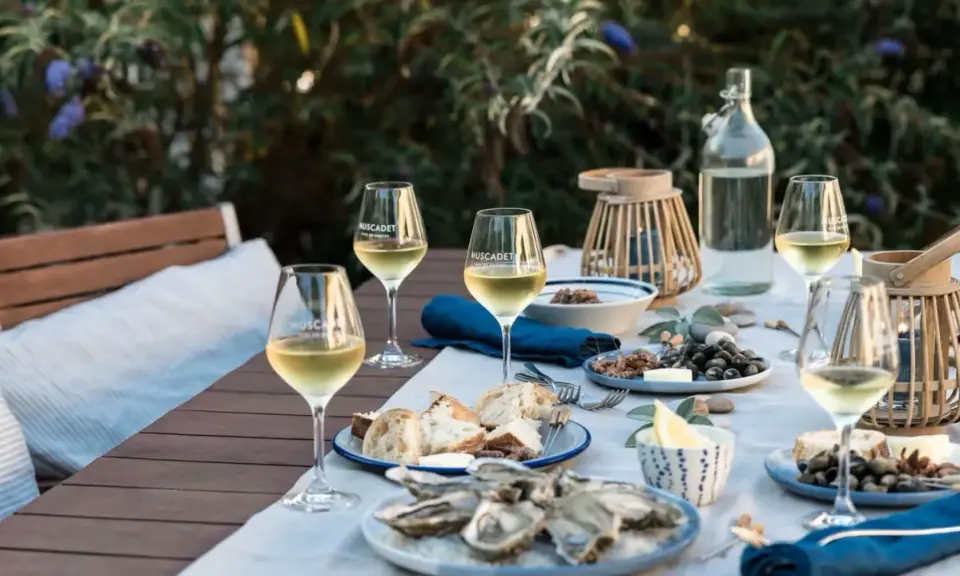 Ein gedeckter Tisch im Freien mit Austern, Brot und Gläsern voller Muscadet, einem Wein aus der Melon de Bourgogne Traube.