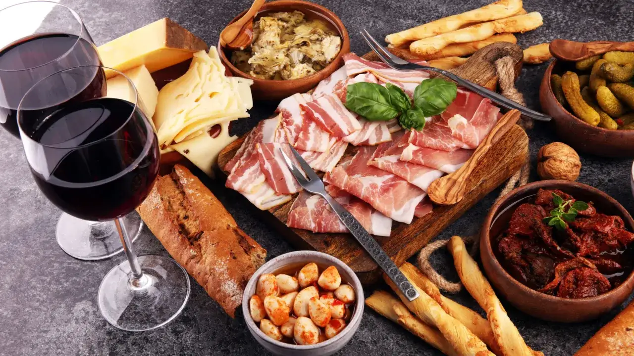 Zwei Gläser Rotwein, Käse, Brot, Schinken und Speck – ein Genuss für Liebhaber von wein trocken.