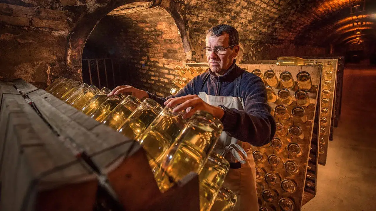 Mann in Keller mit vielen Champagnerflaschen in Holzgestellen.