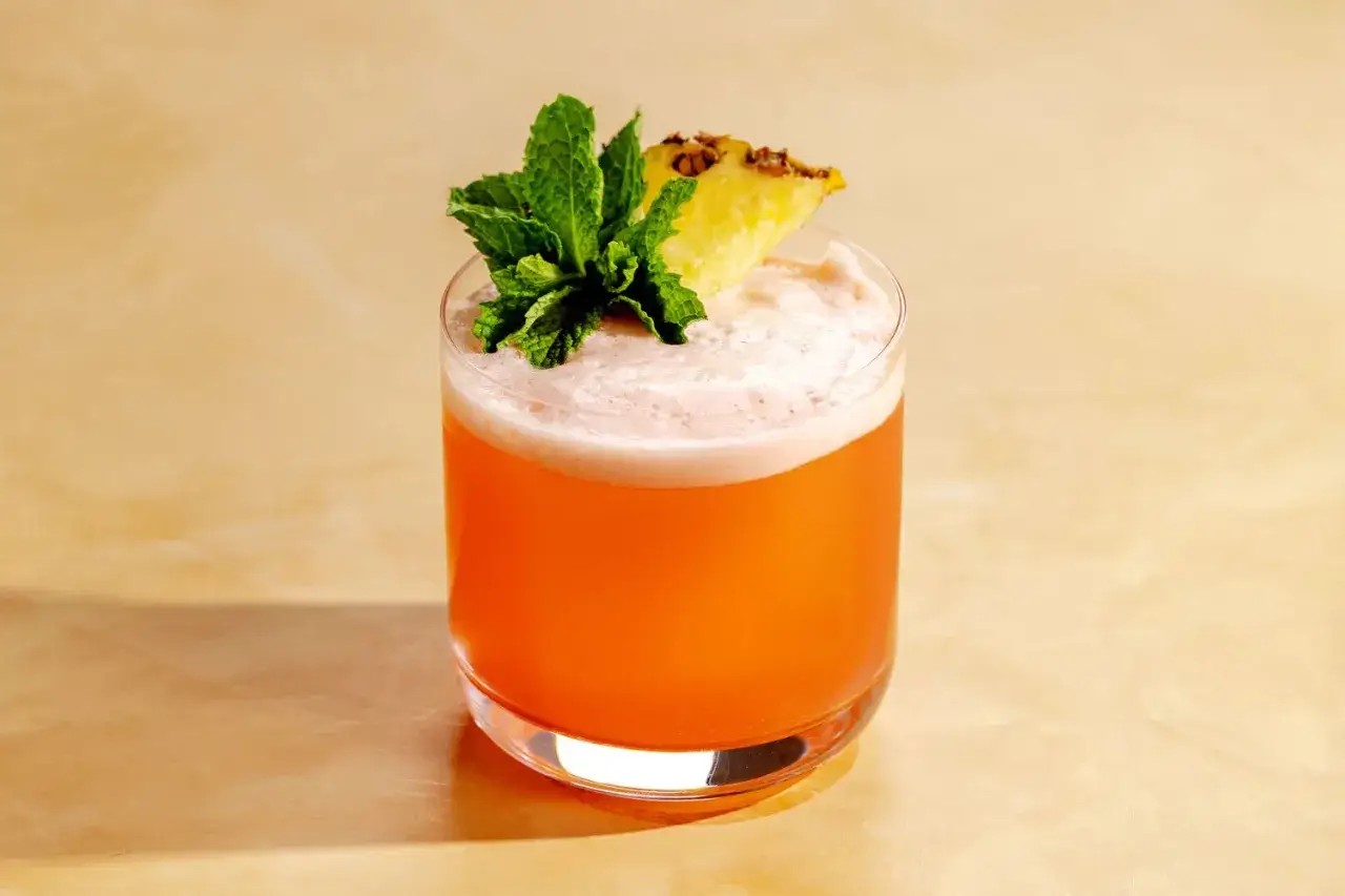 Ein orangefarbener Cocktail in einem Glas, garniert mit Minze und Ananas.