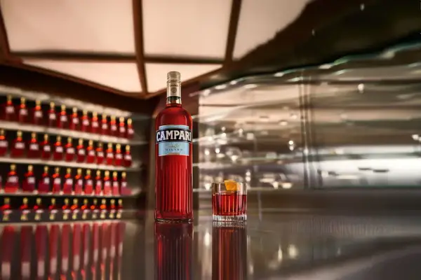 Eine Flasche Campari und ein Glas mit dem roten Aperitif stehen auf einer glänzenden Theke. Die Frage "wie schmeckt Campari?" wird durch den Anblick des ikonischen Getränks aufgeworfen.